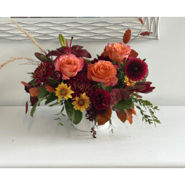Orange and burgundy floral arrangement in a white container