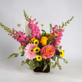 Mixed bouquet with pink snapdragons, roses, gerbera daisies, and yellow daisies in a dark vase