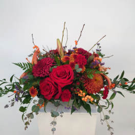 Red floral arrangement with two tall red candles in a white container