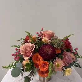 Mixed bouquet of pink, orange, and red flowers in a low metal vase