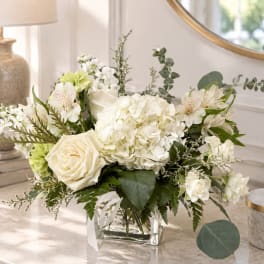 White floral arrangement in a clear glass vase with roses and hydrangeas