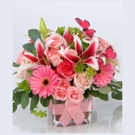 Pink and white flower arrangement in a glass vase with a ribbon and butterfly picks