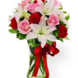 Bouquet of pink roses and white lilies with red ribbon in a glass vase