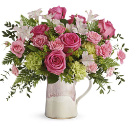 Pink roses and pale lilies arranged in a ceramic pitcher vase