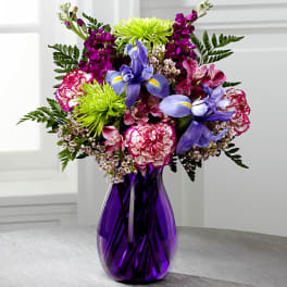 Mixed bouquet of purple, pink, and blue flowers in a purple glass vase
