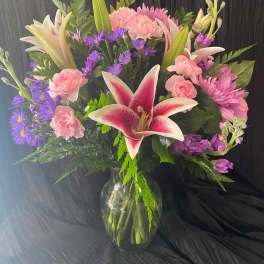 Bouquet of pink lilies, carnations, and purple daisies in a glass vase