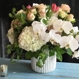 White orchids and pale roses arranged in a ribbed white vase
