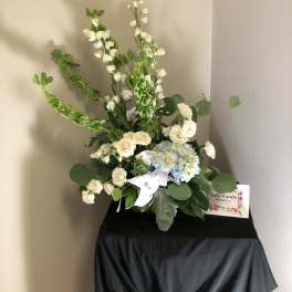 Tall floral arrangement with white blooms, blue hydrangea, and a white ribbon
