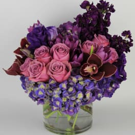 Pink roses and purple flowers arranged in a clear glass vase