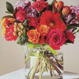 Mixed bouquet of red, orange, and pink flowers in a clear glass vase