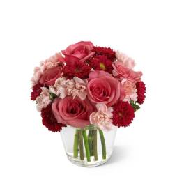 Short arrangement of pink roses, pale carnations, and red mums in a clear glass vase