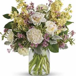 Arrangement of white peonies, yellow stock, and pink filler flowers in a clear glass jar vase