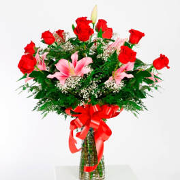 Bouquet of red roses and pink lilies in a glass vase with a red ribbon