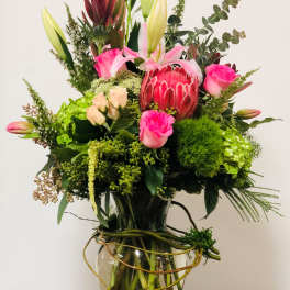Tall mixed bouquet in a glass vase with pink lilies, roses, and a protea