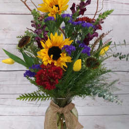 Mixed bouquet with sunflowers, tulips, and red blooms in a glass vase