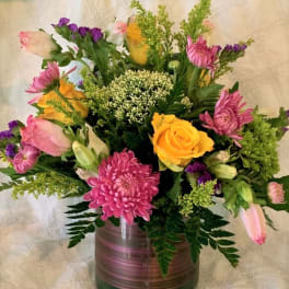 Mixed bouquet of pink, yellow, and purple flowers in a glass vase