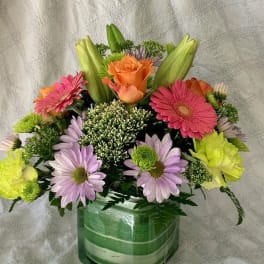 Mixed bouquet in a green glass vase with pink, orange, and lavender flowers