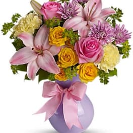 Pink lilies and roses in a lavender vase with a pink ribbon