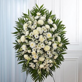 Large white funeral spray with mixed flowers and palm leaves on an easel