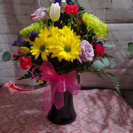 Bouquet of yellow daisies, roses, and tulips in a black vase with a pink bow