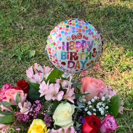 Birthday balloon above a colorful rose bouquet on grass