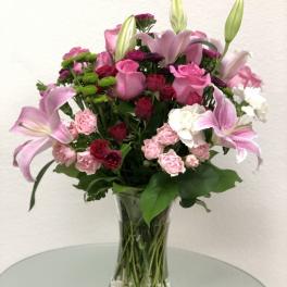 Pink lilies and roses arranged in a clear glass vase