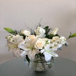 White lilies and roses arranged in a clear glass bowl vase