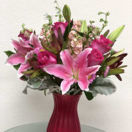 Pink lilies and roses arranged in a red glass vase