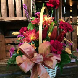 Basket arrangement of red, pink, and yellow flowers with a large ribbon bow
