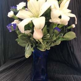 White lilies and purple filler flowers in a blue glass vase