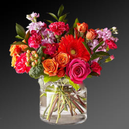 Mixed bouquet of roses, gerbera daisies, and carnations in a glass vase