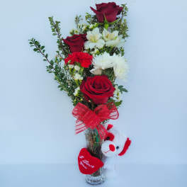 Red roses and white flowers in a clear vase with a plush teddy bear