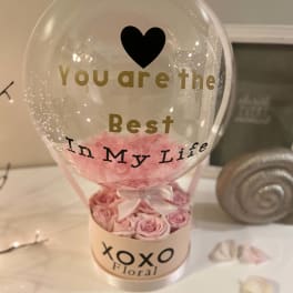 Pink roses in a clear balloon gift box with a heart and text