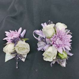 Two lavender and white floral corsages on a dark fabric background