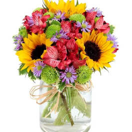 Mixed bouquet of sunflowers, red flowers, and purple daisies in a glass vase