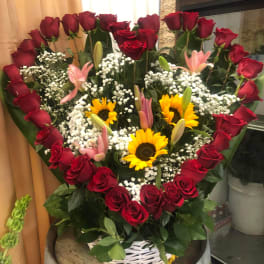 Heart-shaped bouquet of red roses with sunflowers and pink lilies in a white basket