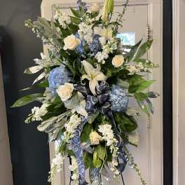 Tall floral spray with blue hydrangeas, white lilies, and cream roses on an easel