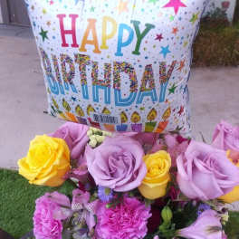 Birthday balloon above a bouquet of roses and pink flowers in a glass vase