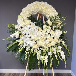 Large white funeral wreath on an easel with lilies and roses