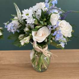 White roses and blue flowers arranged in a glass vase