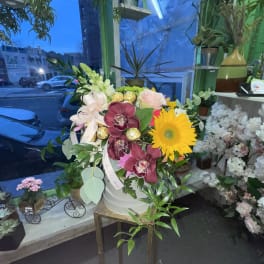 Mixed flower arrangement in a white bucket with a yellow gerbera daisy and orchids