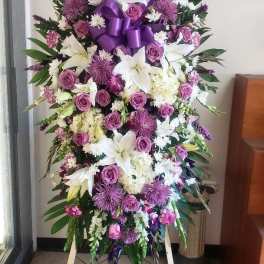 Standing floral spray with white lilies, purple roses, and a purple ribbon