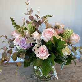 Pastel roses and greenery arranged in a clear glass vase