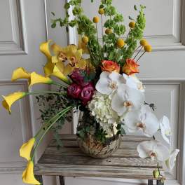 Tall mixed floral arrangement with yellow calla lilies, orchids, and roses in a metallic vase