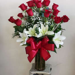 Red roses and white lilies arranged in a tall glass vase with a red bow.