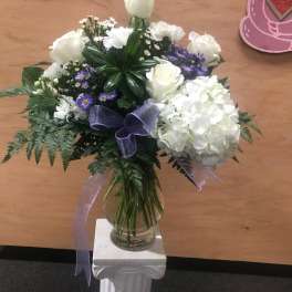 White rose and hydrangea bouquet in a glass vase with purple ribbon
