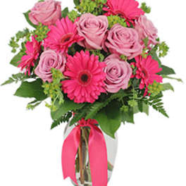 Pink roses and gerbera daisies in a glass vase with a pink ribbon