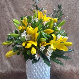 Yellow lilies and white flowers arranged in a white textured vase