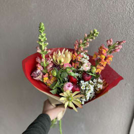 Handheld bouquet with mixed pink, red, and yellow flowers wrapped in red paper