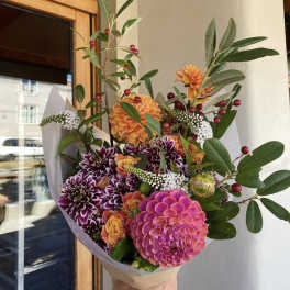 Handheld bouquet of pink, orange, and purple flowers with greenery